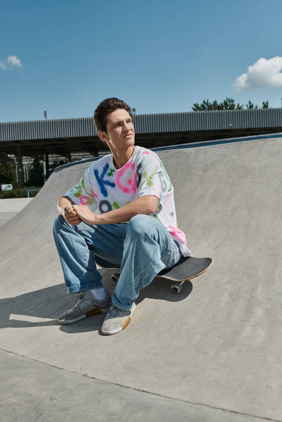 Un joven patinador se sienta con confianza en su monopatín en un colorido parque de skate en un día soleado. - Foto, Imagen