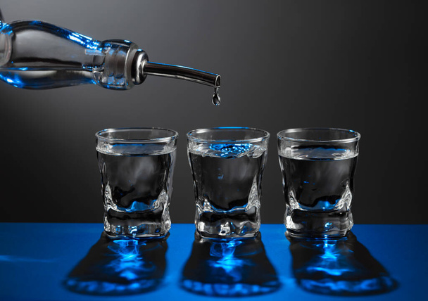 Votka şişeden koyu bir arka planda bir bardağa dökülüyor. Mavi arka ışık. Boşluğu kopyala. - Fotoğraf, Görsel