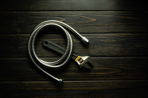 Гибкий шланг и регулируемый универсальный ключ для ремонта на черном винтажном столе. - Фото, изображение