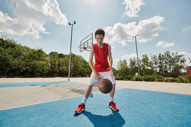 Egy fiatalember kosárlabdát tart, miközben a pályán áll, készülve a játékra.. - Fotó, kép