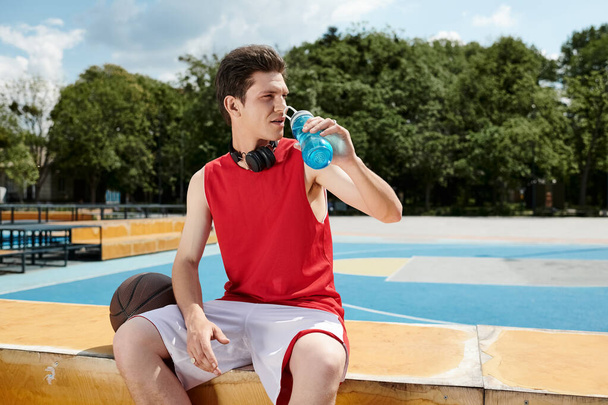 Mladý muž sedí na římse a pije z láhve s vodou za slunečného dne.. - Fotografie, Obrázek