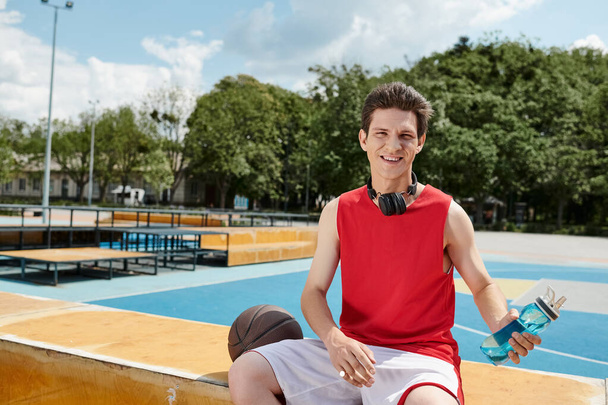 Kırmızı tişörtlü bir adam basketbol sahasının yanında oturmuş huzurlu bir anın tadını çıkarıyor.. - Fotoğraf, Görsel