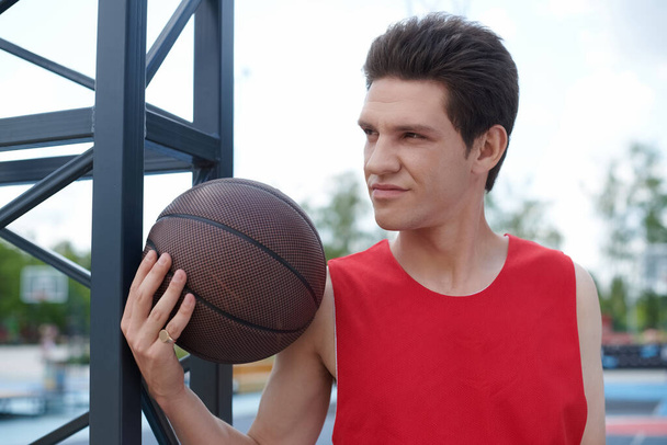 Ein Mann im feuerroten Hemd dribbelt an einem sonnigen Sommertag gekonnt einen Basketball im Freien. - Foto, Bild