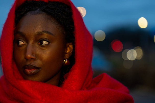 This image captures a side-profile of a young woman looking into the distance, her expression contemplative and serene. She is wrapped in the same vibrant red scarf as before, contrasting dramatically - Photo, Image