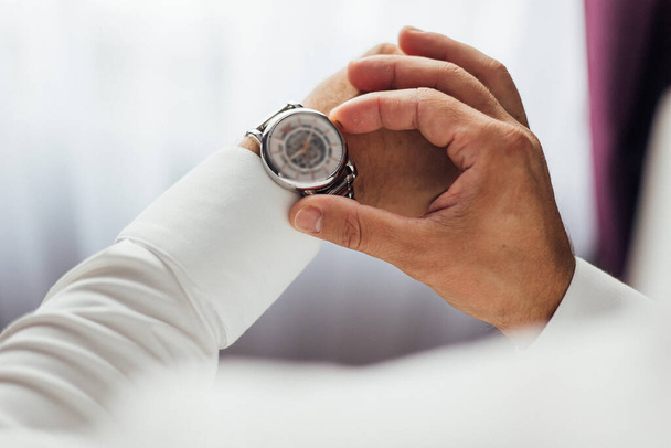 бізнесмен перевіряє час на зап'ясті годинник, чоловік кладе годинник на руку, підготуватися вранці перед церемонією одруження
 - Фото, зображення