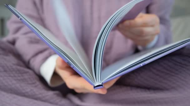 Una mujer en pijama púrpura hojea un libro. - Imágenes, Vídeo