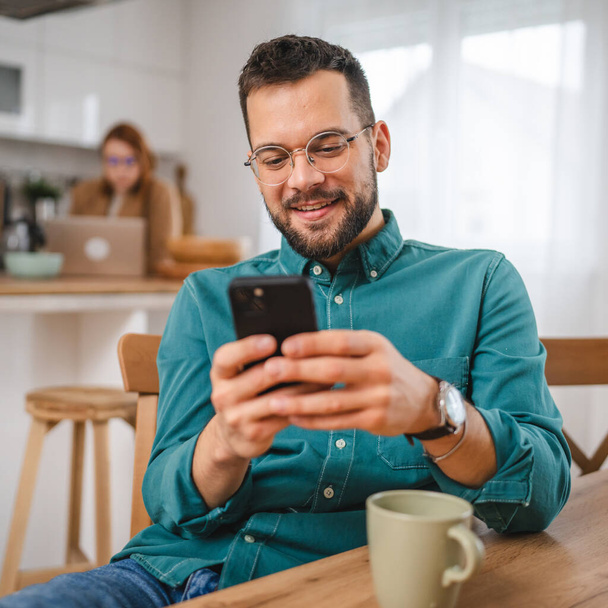 чоловік в окулярах стоїть вдома використовує мобільний телефон смс-повідомлення - Фото, зображення