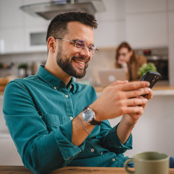 férfi szemüveges állni otthon használat mobiltelefon sms SMS-ezés - Fotó, kép