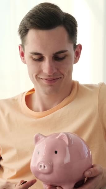 Homem caucasiano, espalhando alegria como ele meticulosamente coloca moedas em seu banco porquinho em casa. Com um sorriso no rosto, ele abraça a responsabilidade financeira e a satisfação de salvar. - Filmagem, Vídeo