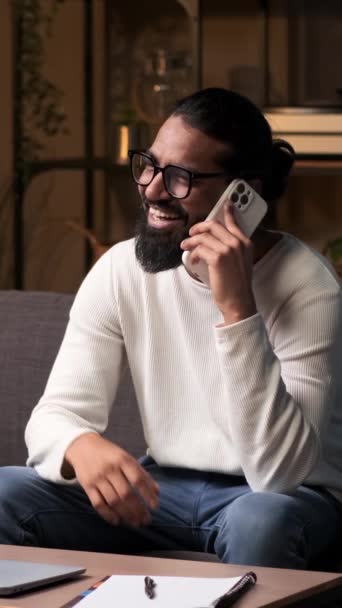 Spokojený muž vede telefonickou konverzaci v obýváku. Jeho radostné výrazy vyjadřují pocit štěstí, vytvářejí rozkošnou scénu spojitosti a pozitivity v klidném prostředí. - Záběry, video