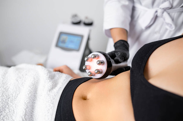 RF body cavitation lifting procedure is employed at the beauty salon to aid a young woman in reducing belly fat. - Photo, Image