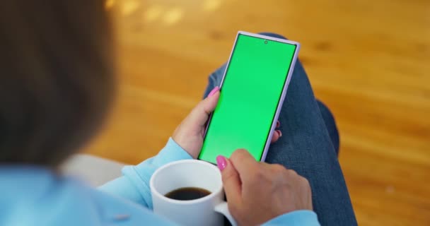 Olkapään yli näkymä nainen käyttää puhelinta, jossa on vihreä ruutu, pitämällä kahvikuppi. Laadukas 4k kuvamateriaalia - Materiaali, video