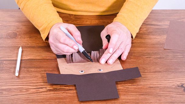 Krok po kroku. Nauczyciel prowadzi zajęcia online poprzez zrobienie papierowej marionetki z brązowej torby, kreatywnie wykorzystując drewnianą powierzchnię jako przestrzeń roboczą. - Zdjęcie, obraz