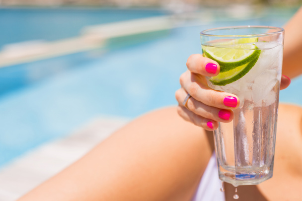 Mujer sosteniendo refrescante bebida fría mientras toma el sol junto a la piscina
 - Foto, imagen
