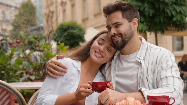 Happy young couple woman boyfriend Caucasian man kissing girlfriend smile drinking coffee cafe city outside hugging cuddle honeymoon sweetheart tenderness dating love romance relationship affectionate - Photo, Image