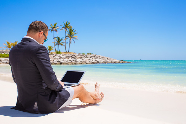 Uomo d'affari che utilizza il computer portatile sulla spiaggia tropicale
 - Foto, immagini