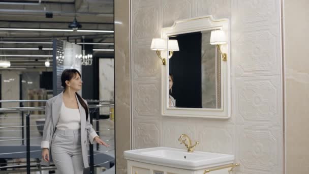 Nainen menossa kylpyhuoneeseen lähellä pesuallas laatta showroom - Materiaali, video