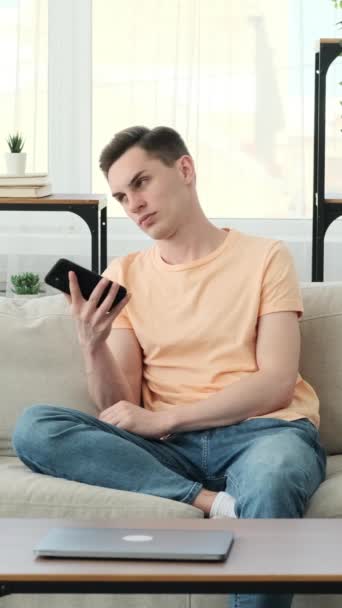 Bored man in casual attire, finds solace in his smartphone. With a disinterested expression, he scrolls through its contents, seeking entertainment or distraction from the monotonous moment. - Footage, Video