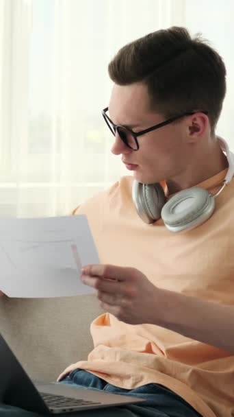 Homem focado em óculos trabalhando com documentos e um laptop na casa aconchegante. Ele navega através de pilhas de papéis, meticulosamente revisando, organizando e analisando documentos importantes. - Filmagem, Vídeo