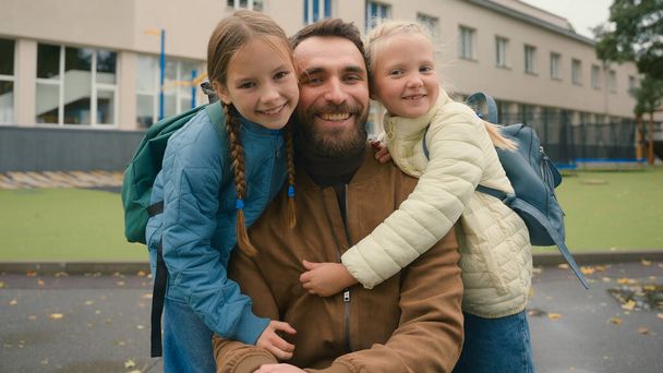 Close up europejski mężczyzna małe dziewczynki ojciec i córki przytulić siostry razem szczęśliwa rodzina uśmiechnięta uczennice dzieci szkoły podstawowej związek więź podejście miłość wsparcie poza miastem - Zdjęcie, obraz