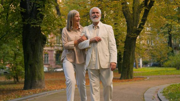 Šťastný zdravý starší důchodce starší běloši prarodiče ženatý muž žena rodina pár chůze drží za ruce mimo městský park vyprávět příběhy mluvit smích společně. Nostalgie vzpomínky odchodu do důchodu - Fotografie, Obrázek