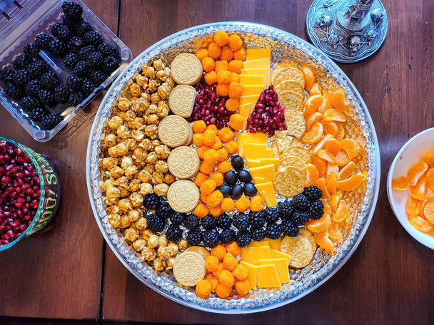 Оживленное блюдо с закусками на праздничном домашнем собрании в Форт-Уэйн, Индиана на Хэллоуин 2021 года, с карамельным попкорном, печеньем, свежими фруктами и сыром. - Фото, изображение