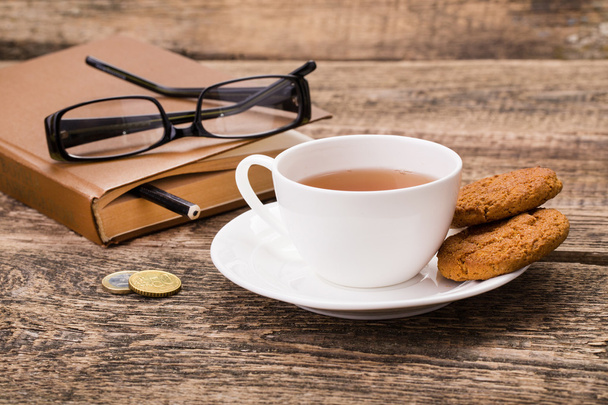ivory tea cup with sweet cookie, glasses, money and book on wood - Foto, Bild