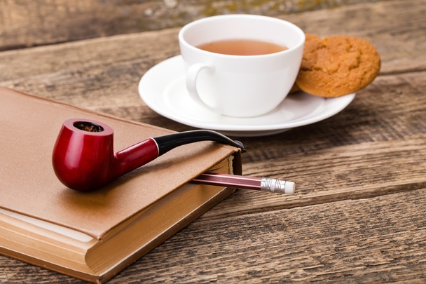 ivory tea cup with sweet cookie, tobacco pipe and book on wooden - Foto, Bild