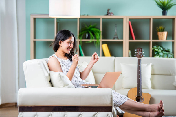 Indian young female with a laptop sitting sofa in a modern living room - Photo, Image