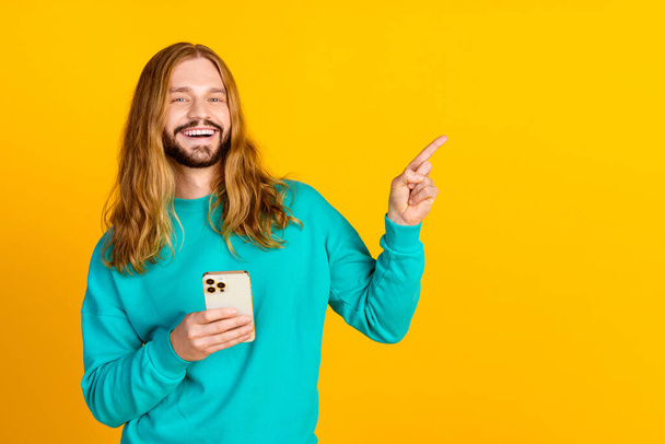 Photo of cheerful guy hold smart phone indicate finger empty space ad isolated on yellow color background. - Foto, imagen