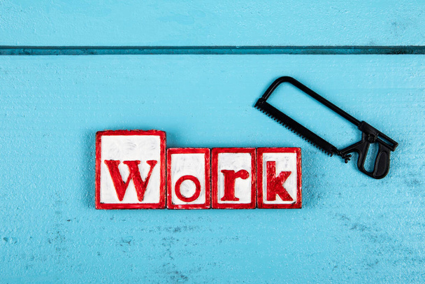WORK. Miniature saw on a blue wooden background. Construction and carpentry concept. - Photo, Image