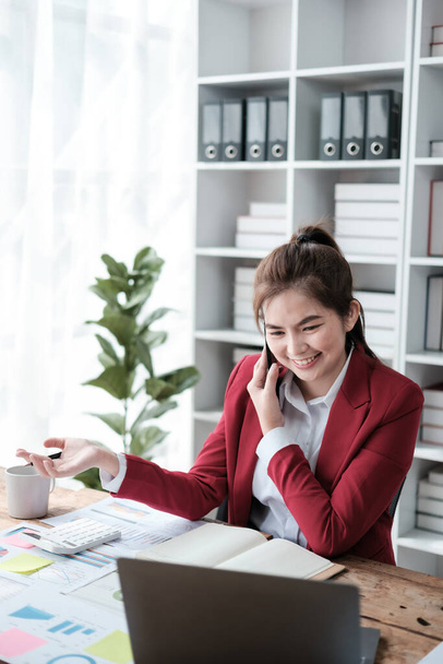 Šťastné asijské obchodní ženy mají radost mluvit na smartphone, tablet, a notebook v domácí kanceláři, na sobě červené apartmá. Kvalitní fotografie - Fotografie, Obrázek