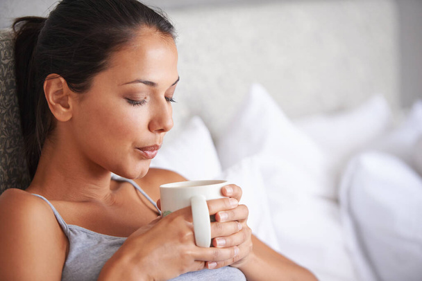 Γυναίκα, καφέ και κρεβάτι για να χαλαρώσετε το πρωί για ξύπνημα και ποτό σε φλιτζάνι για ζεστό και ατμό με μαξιλάρι. Νεαρό άτομο με ποτό για πίπα καφεΐνης το Σαββατοκύριακο για τόνωση σε κούπα με πιτζάμες. - Φωτογραφία, εικόνα