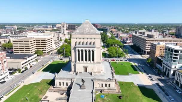 Luchtboog Shot van het majestueuze Indiana War Memorial and Museum, genesteld in het levendige centrum van Indianapolis, met de nadruk op de neoklassieke architectuur en serene stadspark. - Video