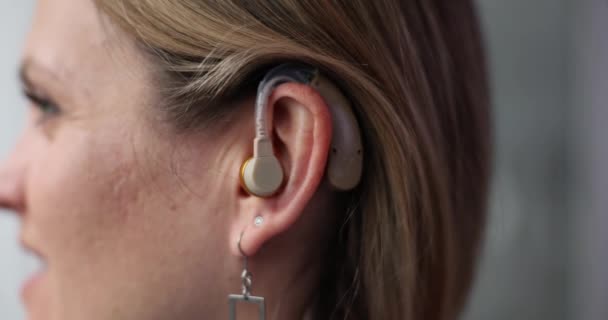 Γυναίκα φοράει ακουστικό βαρηκοΐας για να συμμετάσχει σε συζητήσεις. Θηλυκό βρίσκεται στην αίθουσα εξέτασης βασιζόμενο σε ακουστικό βοήθημα που καθορίζεται στο auricle για αποτελεσματική επικοινωνία - Πλάνα, βίντεο