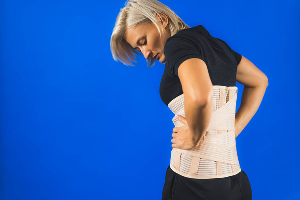 Frau mit einem Korsett auf dem Rücken, um ihren Rücken vor Schmerzen in Rücken und Wirbelsäule zu stützen, medizinisches Konzept, Rückenstütze, Tragen einer Spange zu Hause. Hochwertiges Foto - Foto, Bild