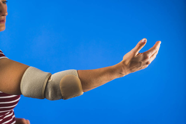 közelkép egy nőről, akinek merevítő van a sérült kezén, kék háttérrel, kezelési koncepció. Kiváló minőségű fénykép - Fotó, kép