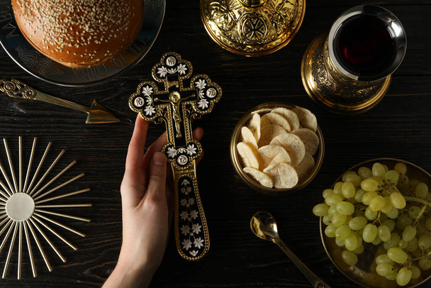 Хліб, хрест у руці, виноград у золотій мисці та чашка вина на дерев'яному фоні, вид зверху - Фото, зображення