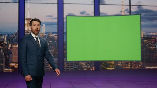 Confident newscast presenter talking daily news in modern tv studio with green screen. Bearded elegant newscaster showing image on mockup monitor. Television newsroom channel with professional anchor. - Photo, Image