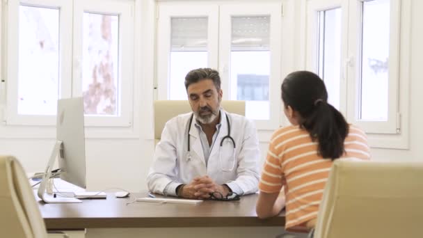 Real time van vrolijke volwassen arts in uniform met stethoscoop rond de nek zitten aan tafel met computer en praten met vrouwelijke patiënt - Video