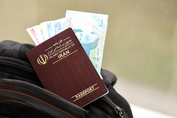 Pasaporte de la República Islámica Roja de Irán con billetes de avión y dinero en mochila turística de cerca. Concepto de turismo y viajes - Foto, imagen
