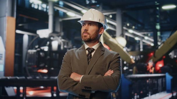 Successful factory owner posing in front modern heavy industrial machinery close up. Portrait of smiling businessman in protective helmet looking camera. Bearded engineer standing on production place. - Foto, Bild