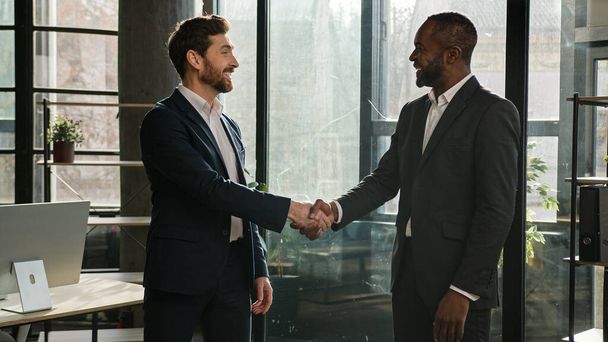 Twee verschillende mannen multiraciale zakenmannen in functie schudden elkaar de hand na succesvolle onderhandelingen. Kaukasische man verkoper handdruk Afro-Amerikaanse zakenpartner klant partnerschap deal overeenkomst - Foto, afbeelding