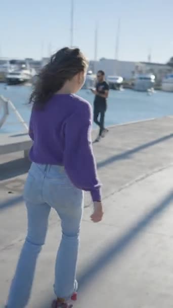 Magányos sötét hajú lány görkorcsolyázik a napfényben hajók kikötőben - FullHD függőleges videó - Felvétel, videó