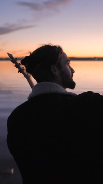 Испанский бородатый гитарист фотографирует себя с гитарой на закате у озера Торревьеха Пинк в Аликанте, Испания - Vertical FullHD video - Кадры, видео