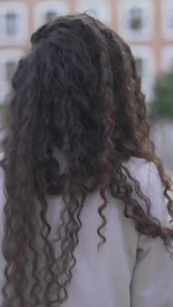 Marokkanische Frau mit langen und lockigen Haaren, die tagsüber im Stadtpark spazieren geht. Rückansicht - Vertikal - Filmmaterial, Video