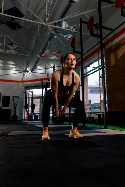 Im Fitnessstudio arbeitet eine Trainerin in schwarzen Leggings und einem Oberteil mit einem Gewicht - Foto, Bild