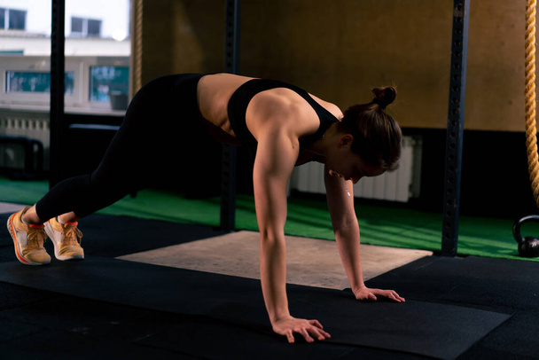 no ginásio uma garota treinador em leggings pretos e um topo faz alongamento no chão - Foto, Imagem