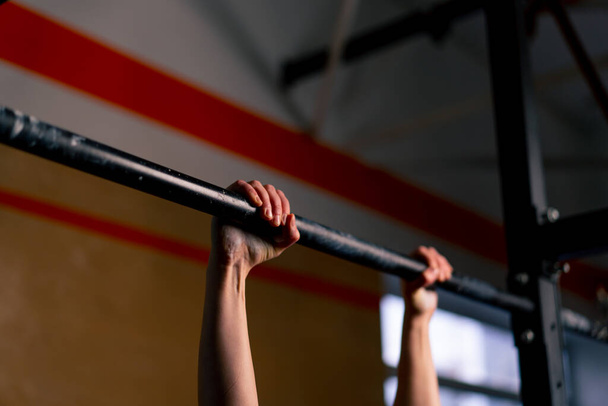 close-up in de sportschool een coach meisje in zwart leggings en een top weegt op de horizontale balk - Foto, afbeelding