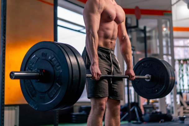 close up in a sports club bald trainer in sports shorts lifts weights on a barbell - Photo, Image
